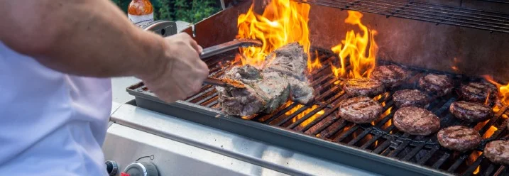 Person grillt Fleisch und Burger mit Grillzange